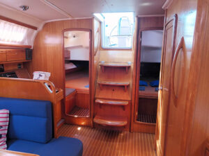 A view of a boat's interior with wooden walls and a glimpse into a cabin. The stairs leading up to the deck are visible, as well as a partially opened door revealing a bed.